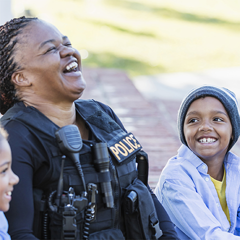 Policewoman laughing on a curb with young children